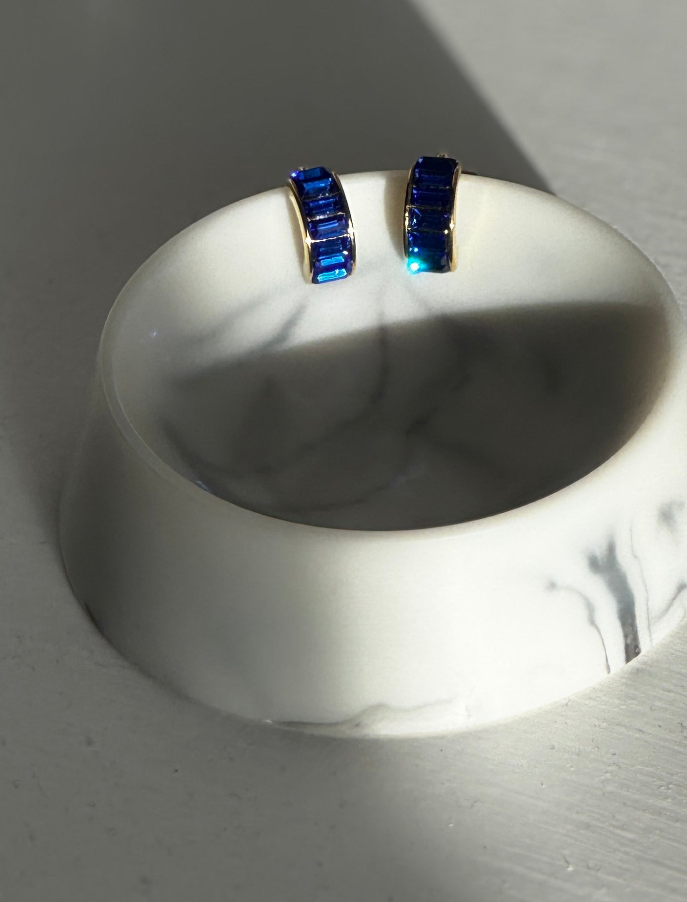 Pair of blue gemstone earrings on a white stand against a gray background