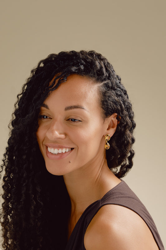 Woman with styled hair smiling against a neutral background wearing Emma Holland earrings