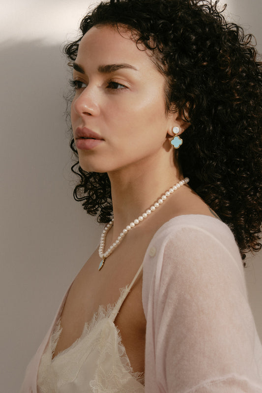 Woman wearing a pearl necklace and earrings against a neutral background
